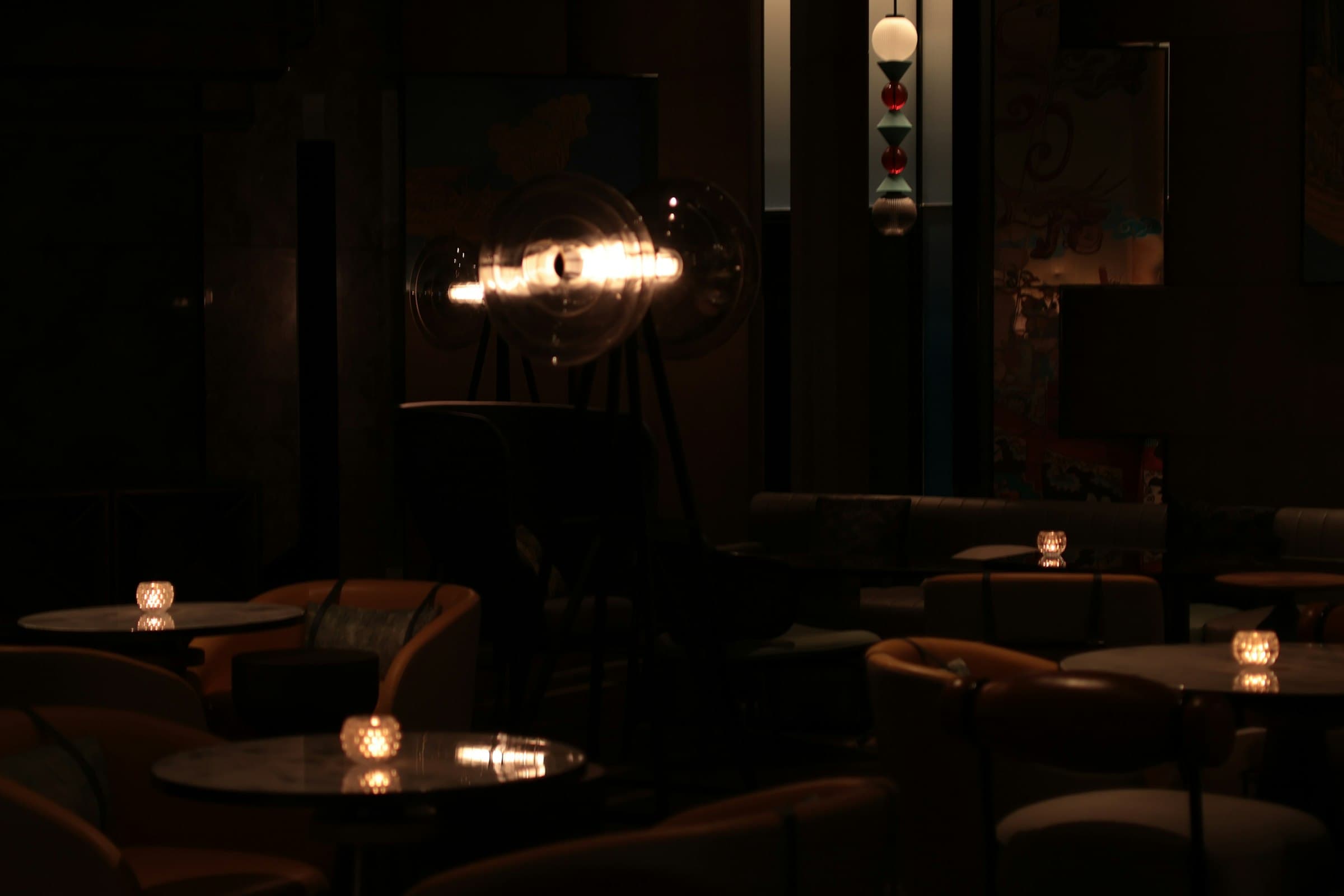 The Vesper room at night — marble tables, leather chairs, votive candles, and one glowing pendant lamp