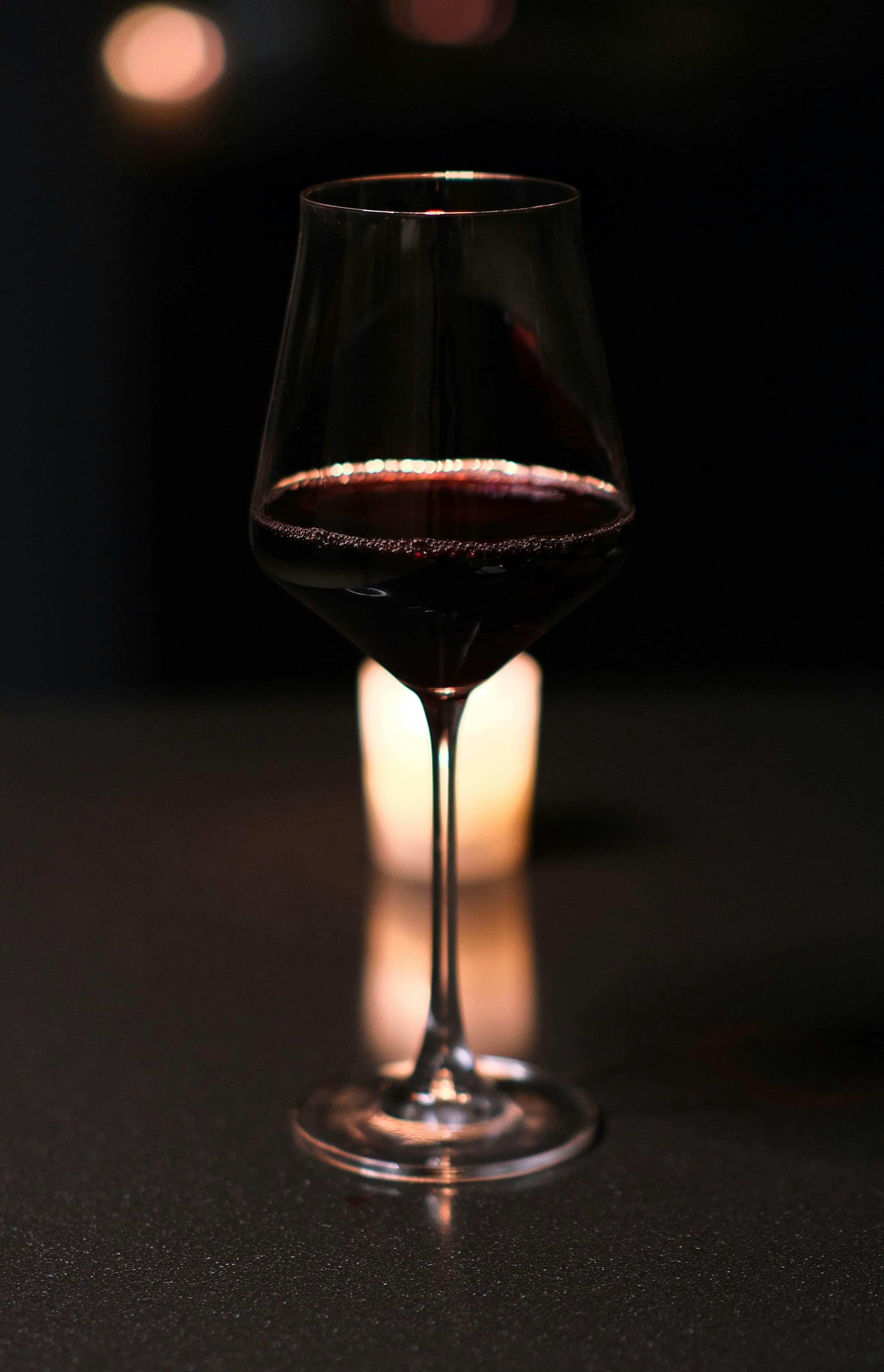 A glass of red wine on a dark counter, lit by a single votive candle