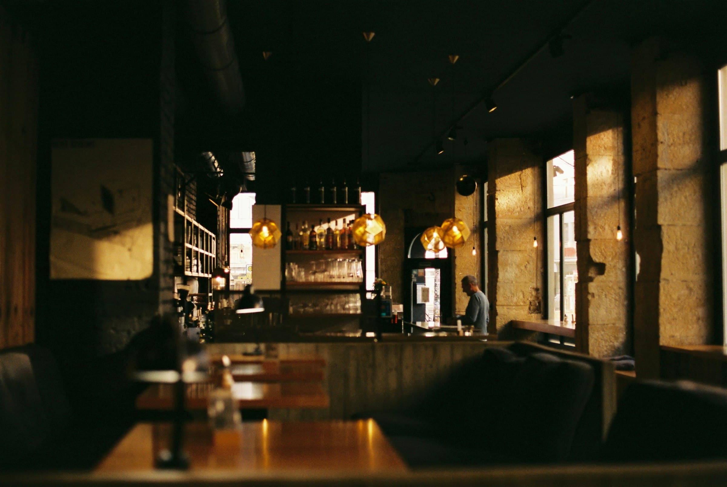 The bar at golden hour — geometric brass pendants, stone pillars, low sun raking through tall windows